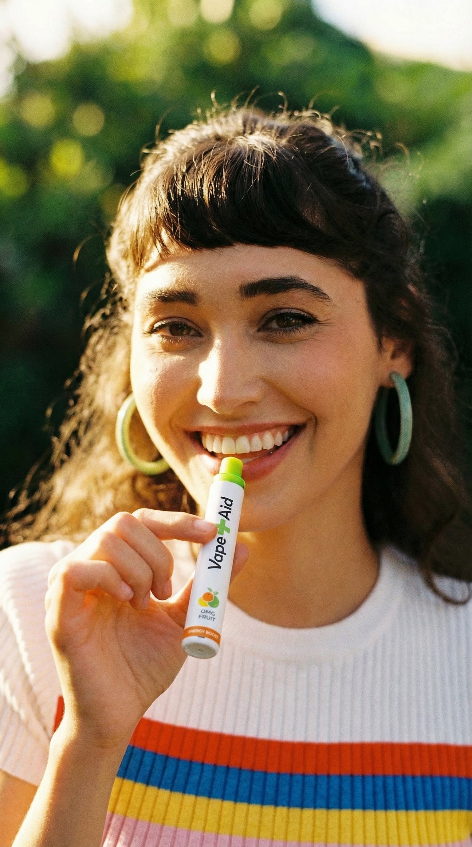 Woman smiling and holding a Vape+Aid diffuser outdoors with greenery in the background