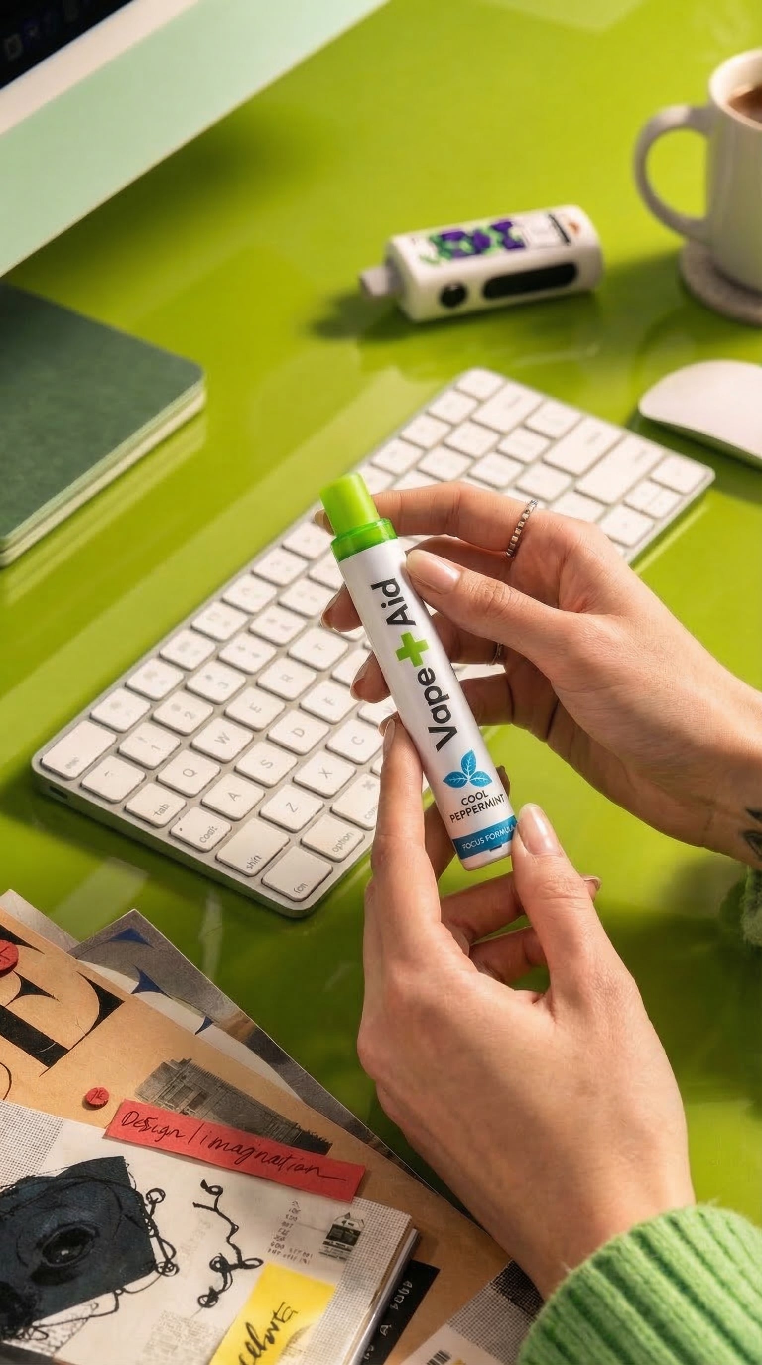 Person holding a Vape+Aid diffuser on a desk with a keyboard and coffee cup in the background