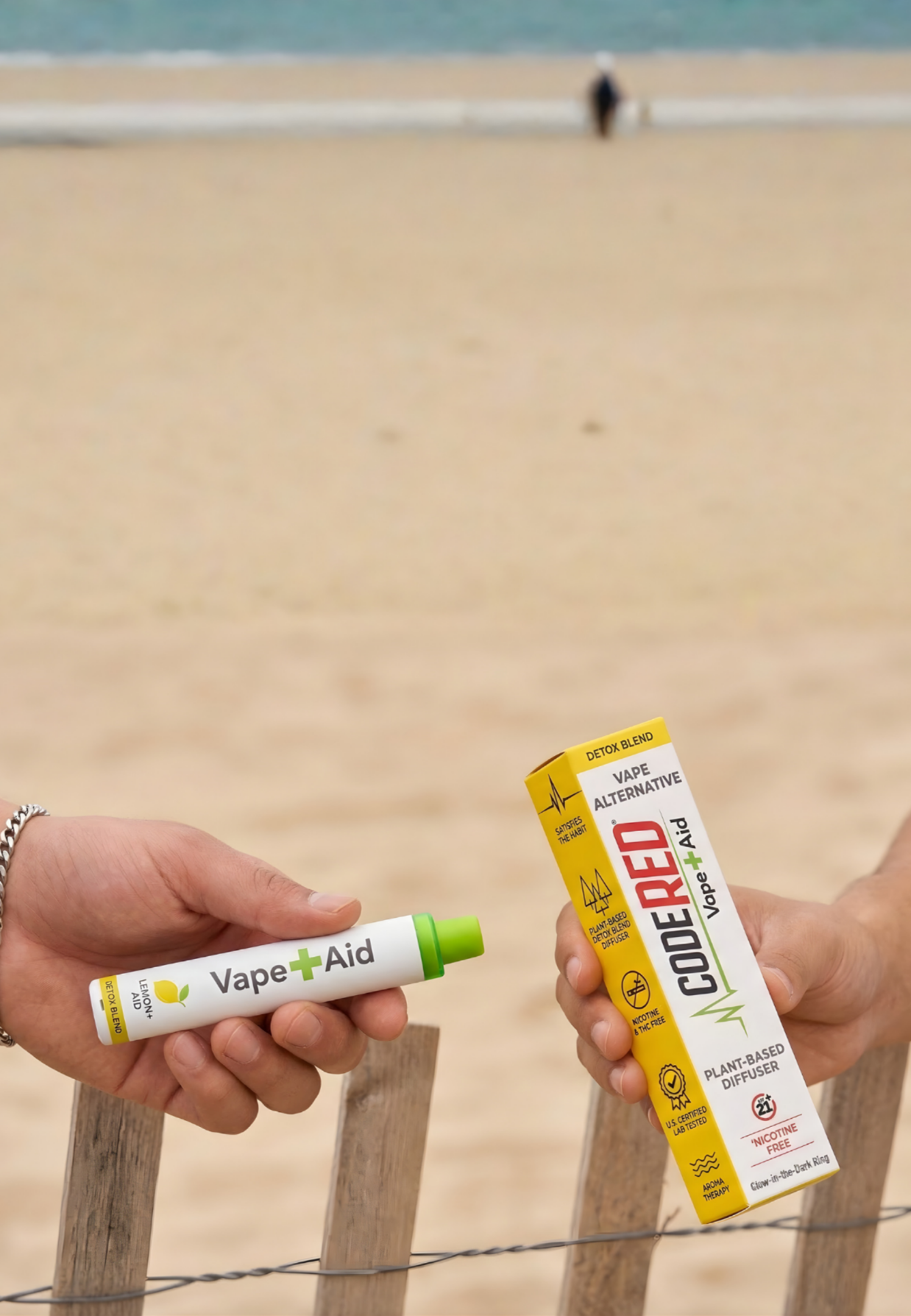 Two hands holding Vape+Aid diffuser and packaging on a beach.